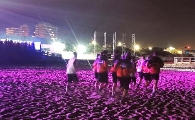Los jugadores corren por la playa con las discotecas de fondo.  @prensariestra