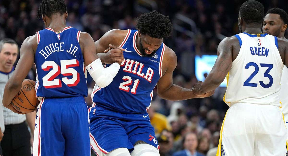 Joel Embiid ayudado por sus compañeros y rivales antes de retirarse lesionado ante los Warriors./AFP