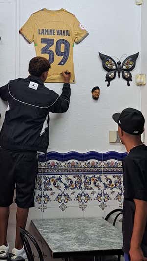 Lamine firma, al lado de su padre, la camiseta colgada en el bar de Carlos. IMAGEN CEDIDA