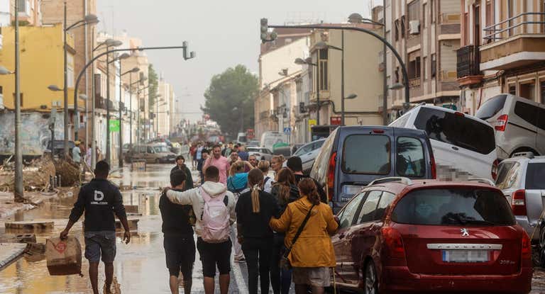 Varias personas junto a coches destrozados tras el paso de la DANA por el barrio de La Torre de Valencia.